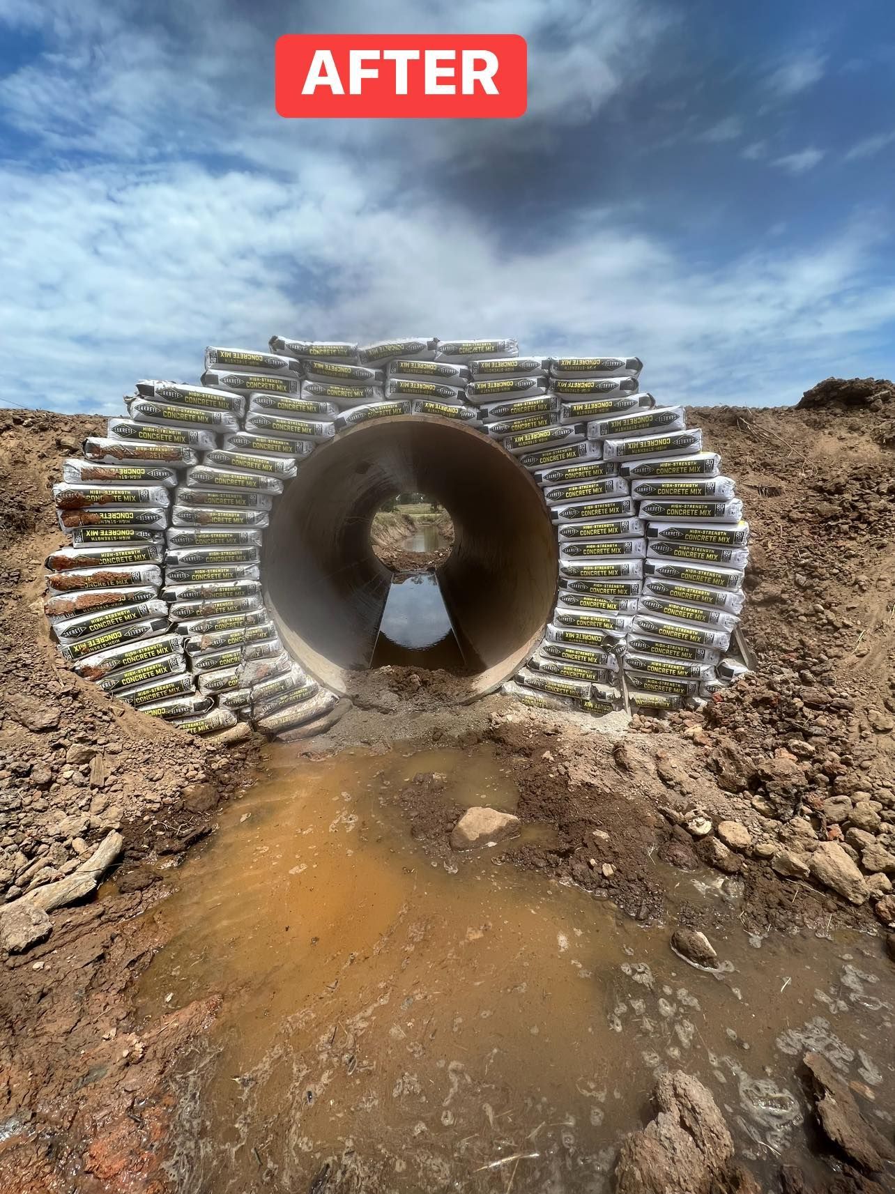 Concrete culvert encased in layers of sandbags, with muddy water flowing through.