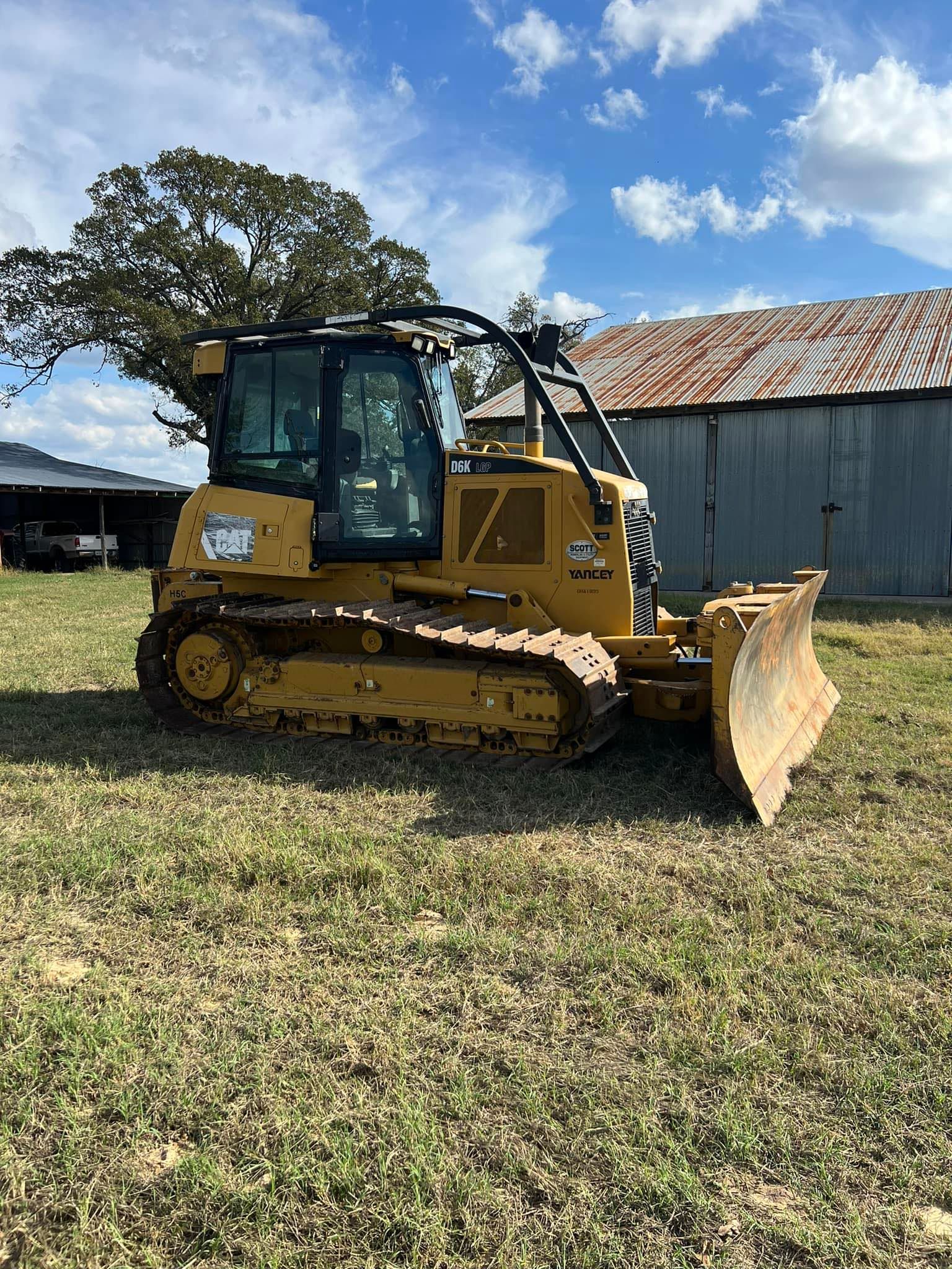 Yellow Caterpillar bulldozer on grassy field with blue sky and shed in the background.