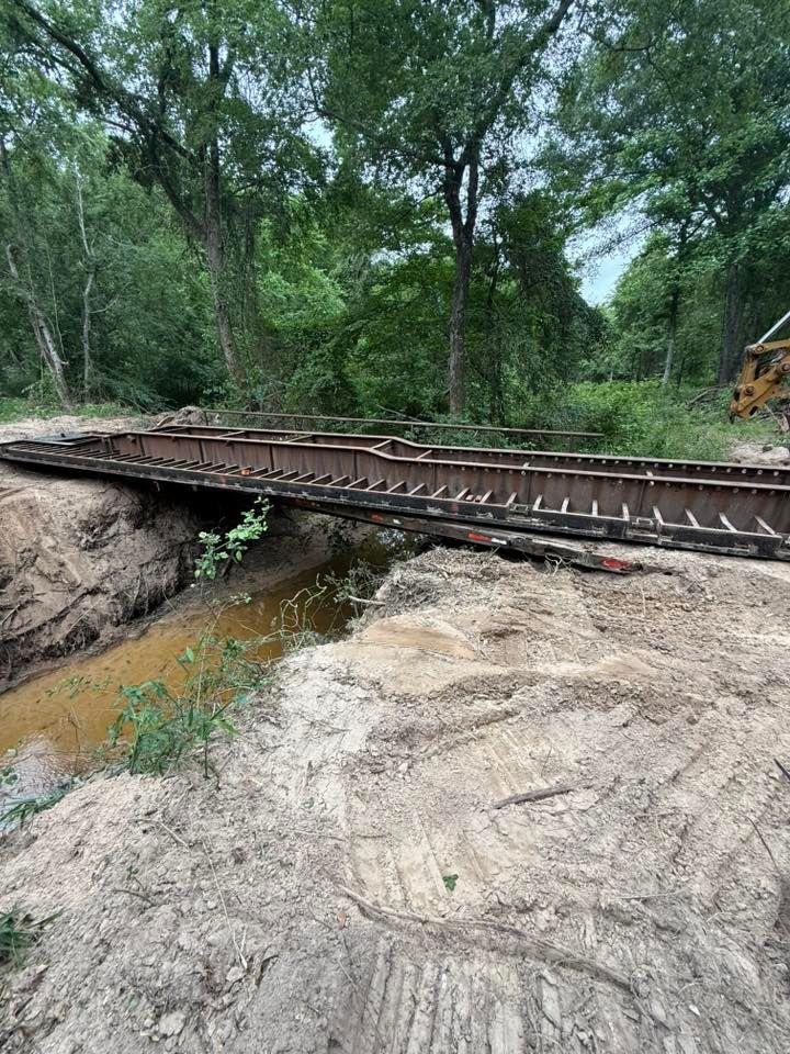 Bridge over a small creek in a wooded area; dirt banks on either side.