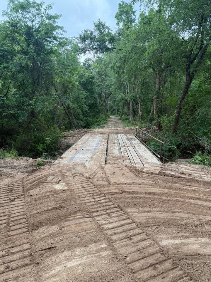 Gravel road leading to a concrete bridge in a wooded area.