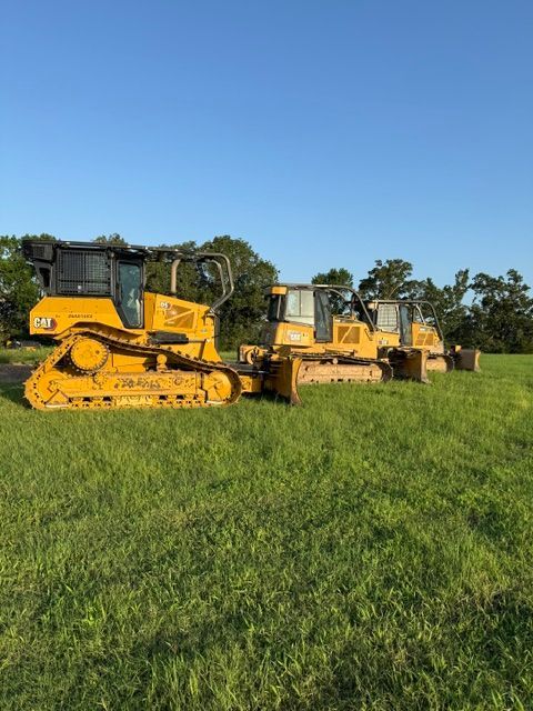 Four yellow bulldozers on a grassy field under a blue sky.