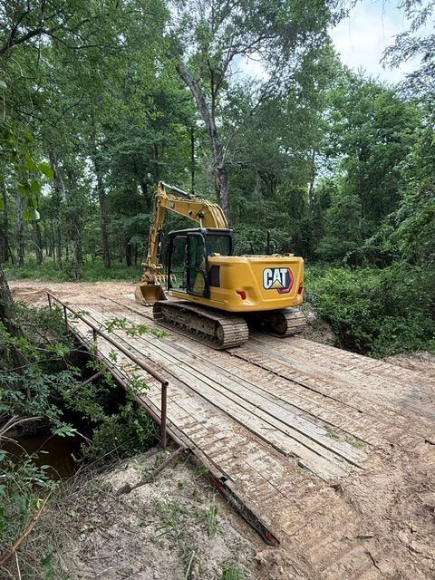 Yellow CAT excavator on a wooden bridge in a wooded area.