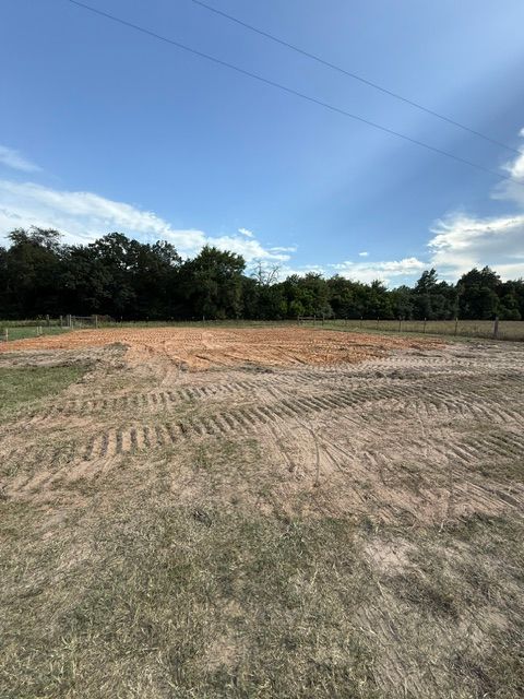 Cleared dirt field with tire tracks, against a tree line and blue sky.