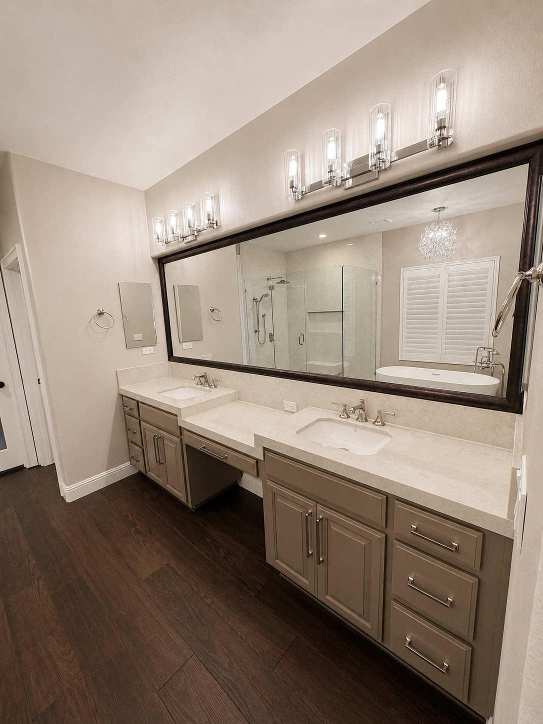 Elegant bathroom vanity with large mirror, double sinks, and dark wood floor under wall sconces