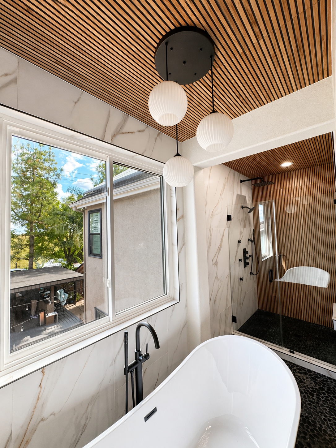 Bright modern bathroom with a freestanding tub, large window, and wood slat ceiling