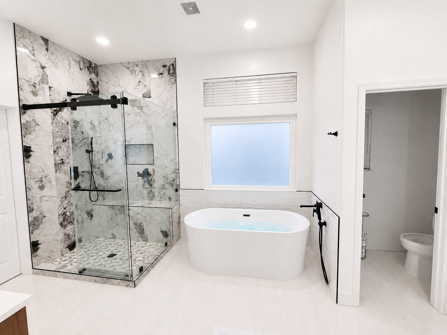 Bright modern bathroom with glass shower, freestanding tub, and adjacent toilet room.