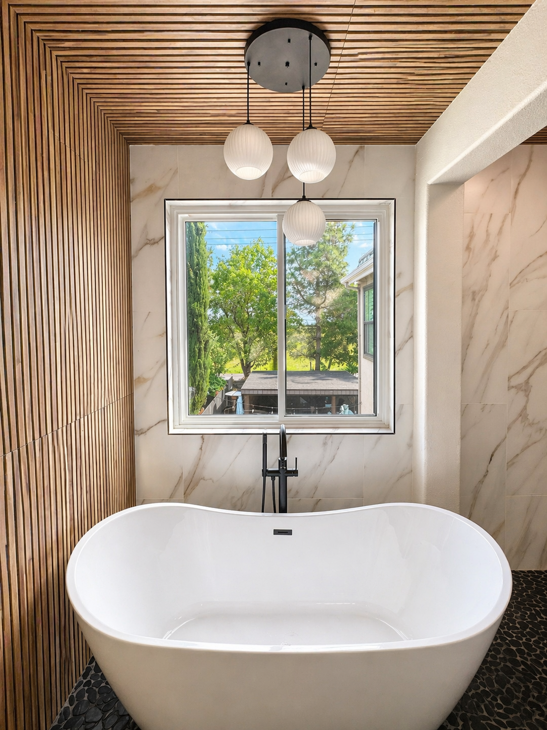 Modern bathroom with a white freestanding tub, wood ceiling, and window overlooking trees