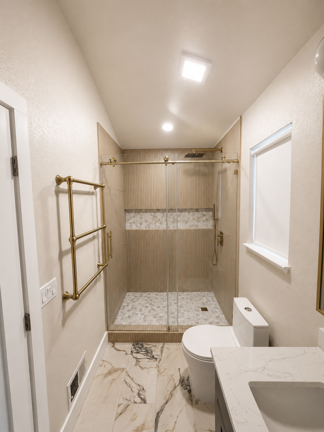 Small beige bathroom with marble tile, walk-in shower, toilet, sink, and brass towel rack.