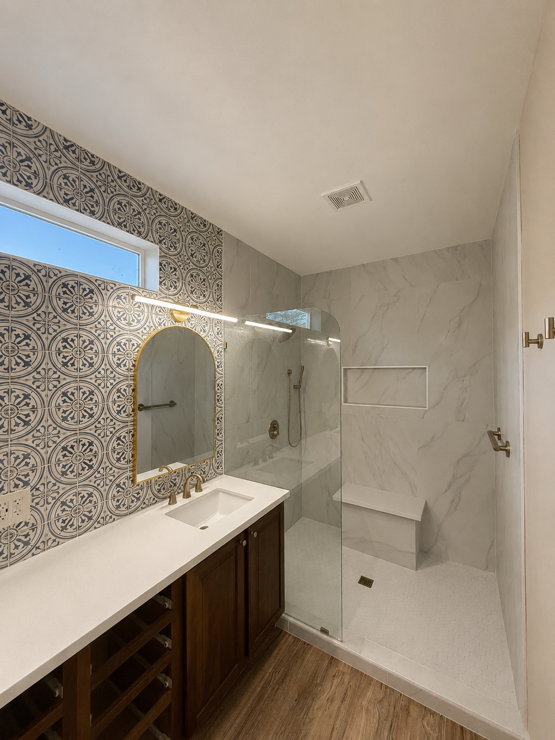 Bathroom with white vanity, arched mirror, and walk-in shower with patterned tile accent wall.