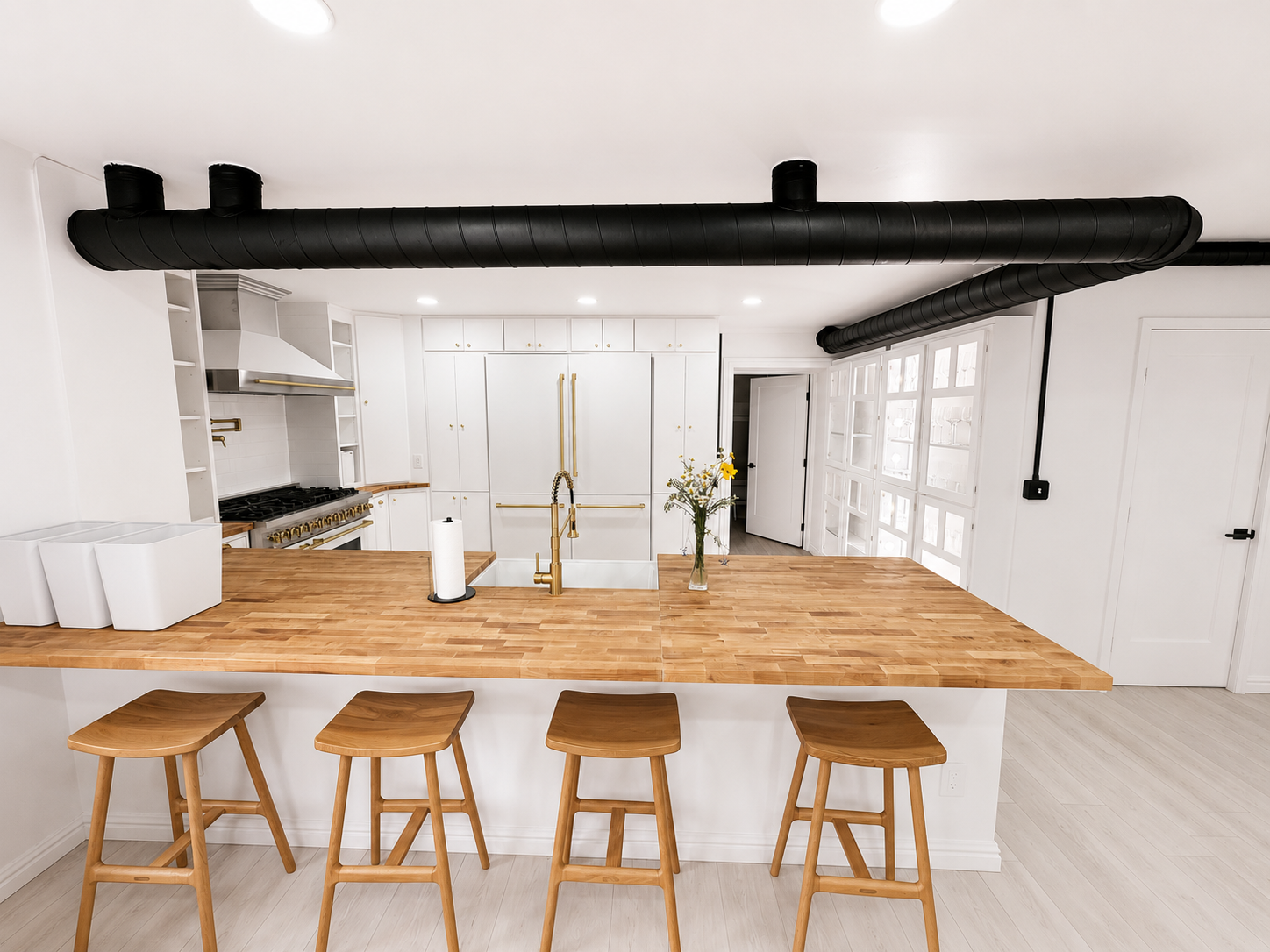Modern white kitchen with wooden island, four stools, black ceiling beams, and pendant lights