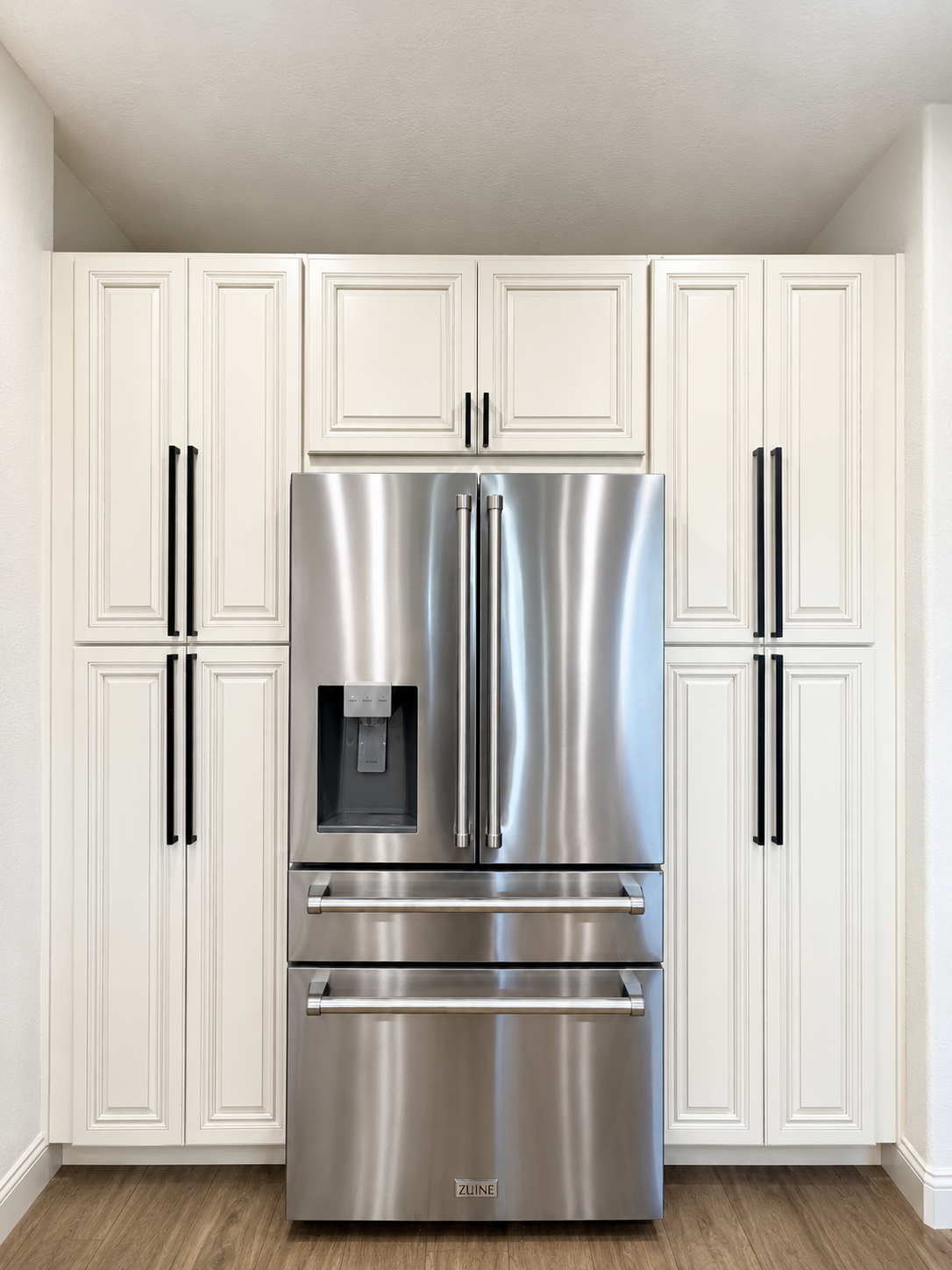Stainless steel French-door refrigerator built into white floor-to-ceiling cabinetry.