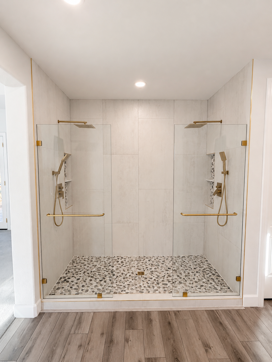 Walk-in shower with white tile walls, pebble floor, gold fixtures, and two glass side panels.