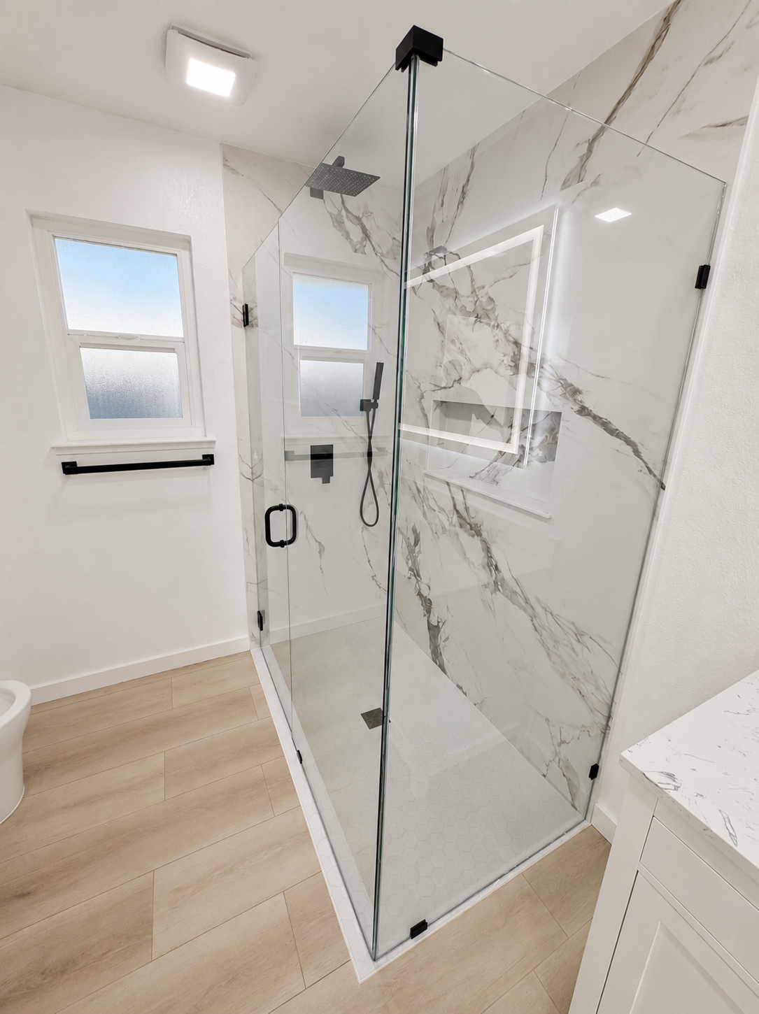 Modern bathroom with glass shower enclosure, marble tile walls, and light wood flooring