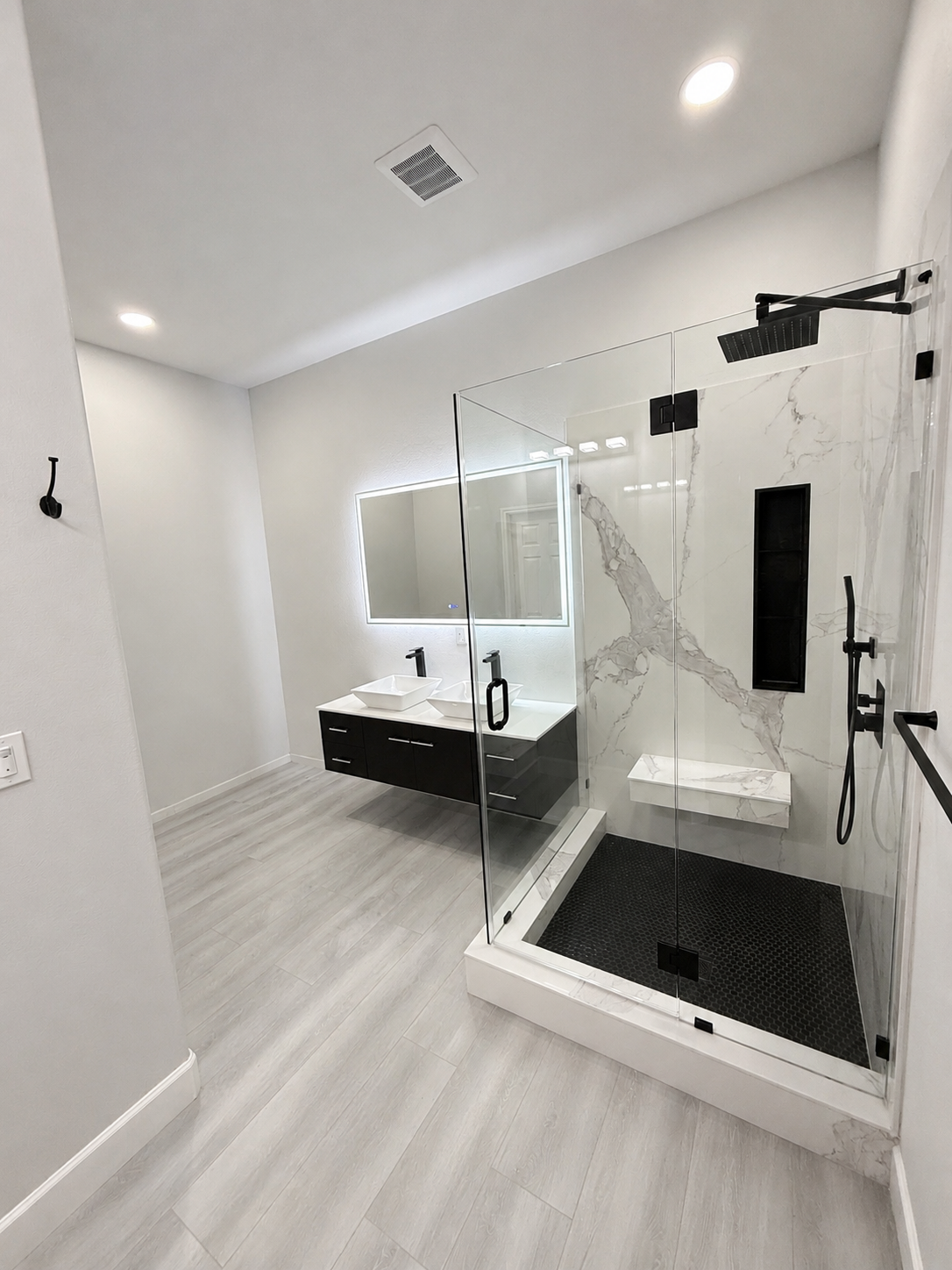 Modern bathroom with double vanity, large mirror, and glass walk-in shower with black tile floor.