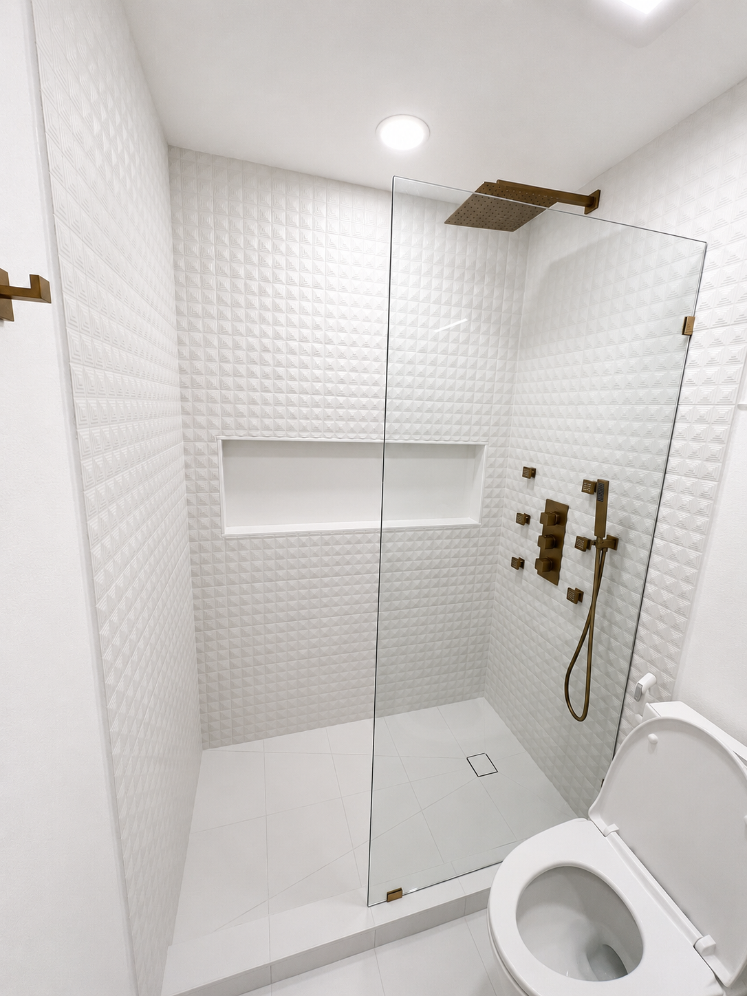 White tiled bathroom with walk-in shower, wall niche, brass fixtures, and toilet in the foreground