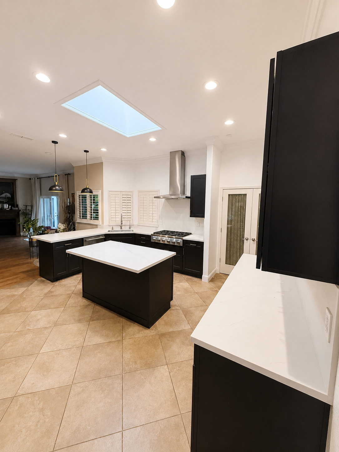 Modern kitchen with black island, white countertops, skylight, and recessed ceiling lights