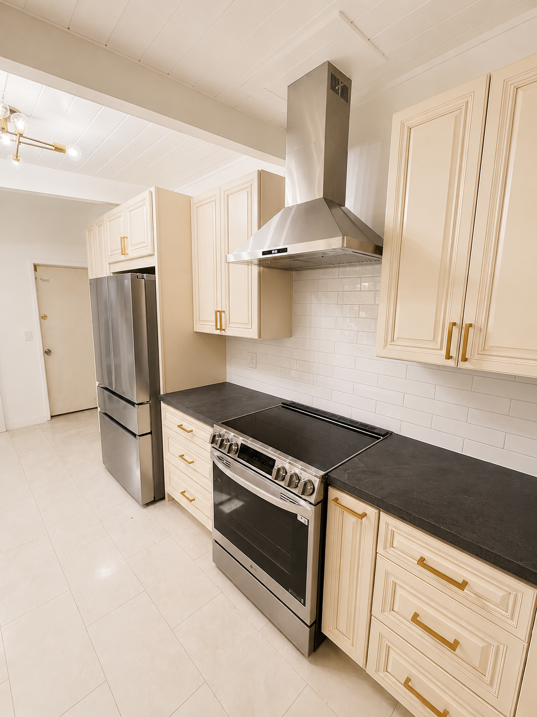 Modern white kitchen with stainless steel fridge, oven, range hood, and black countertops