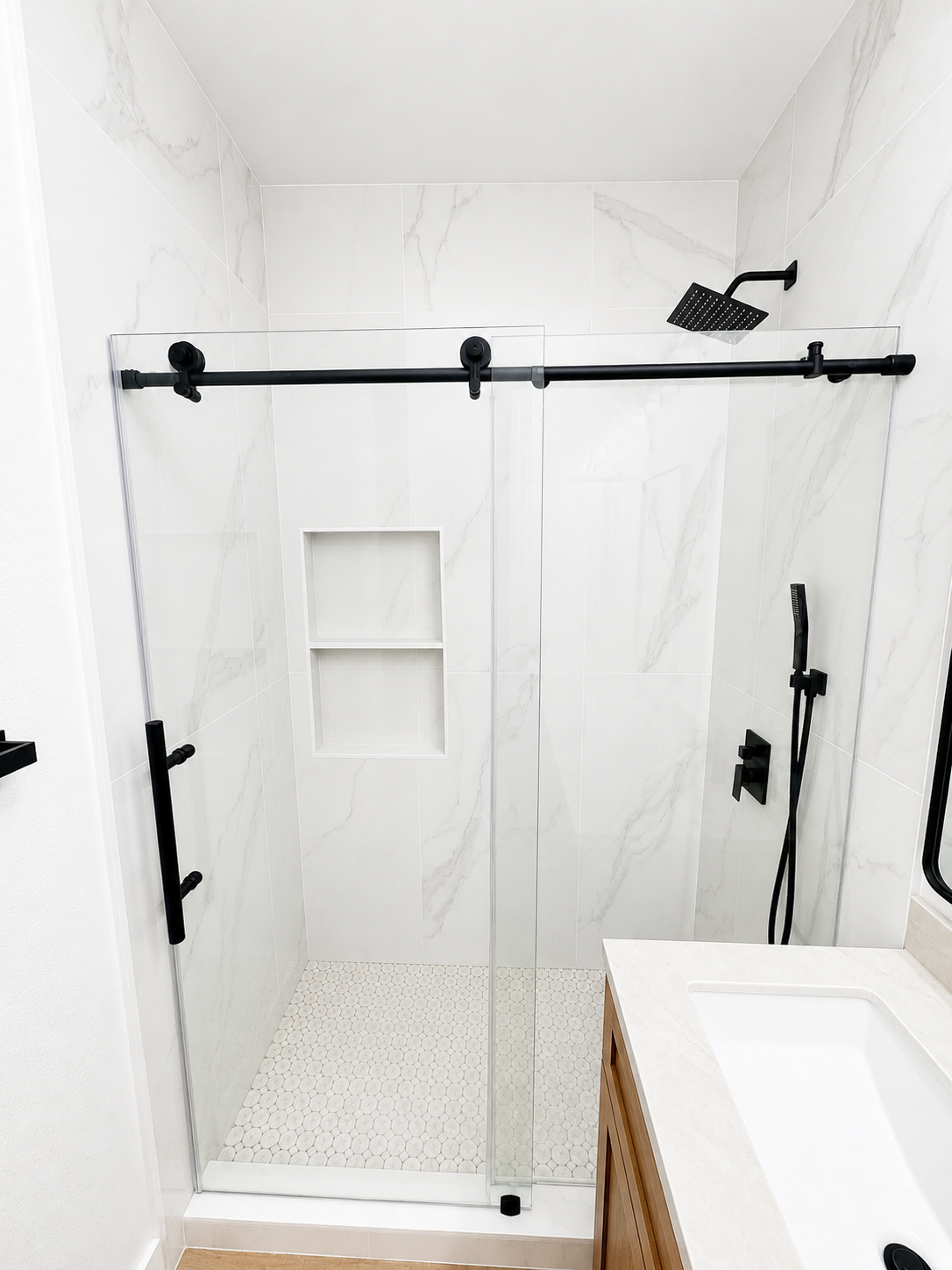 Modern white bathroom with walk-in shower, black hardware, and a built-in wall niche.