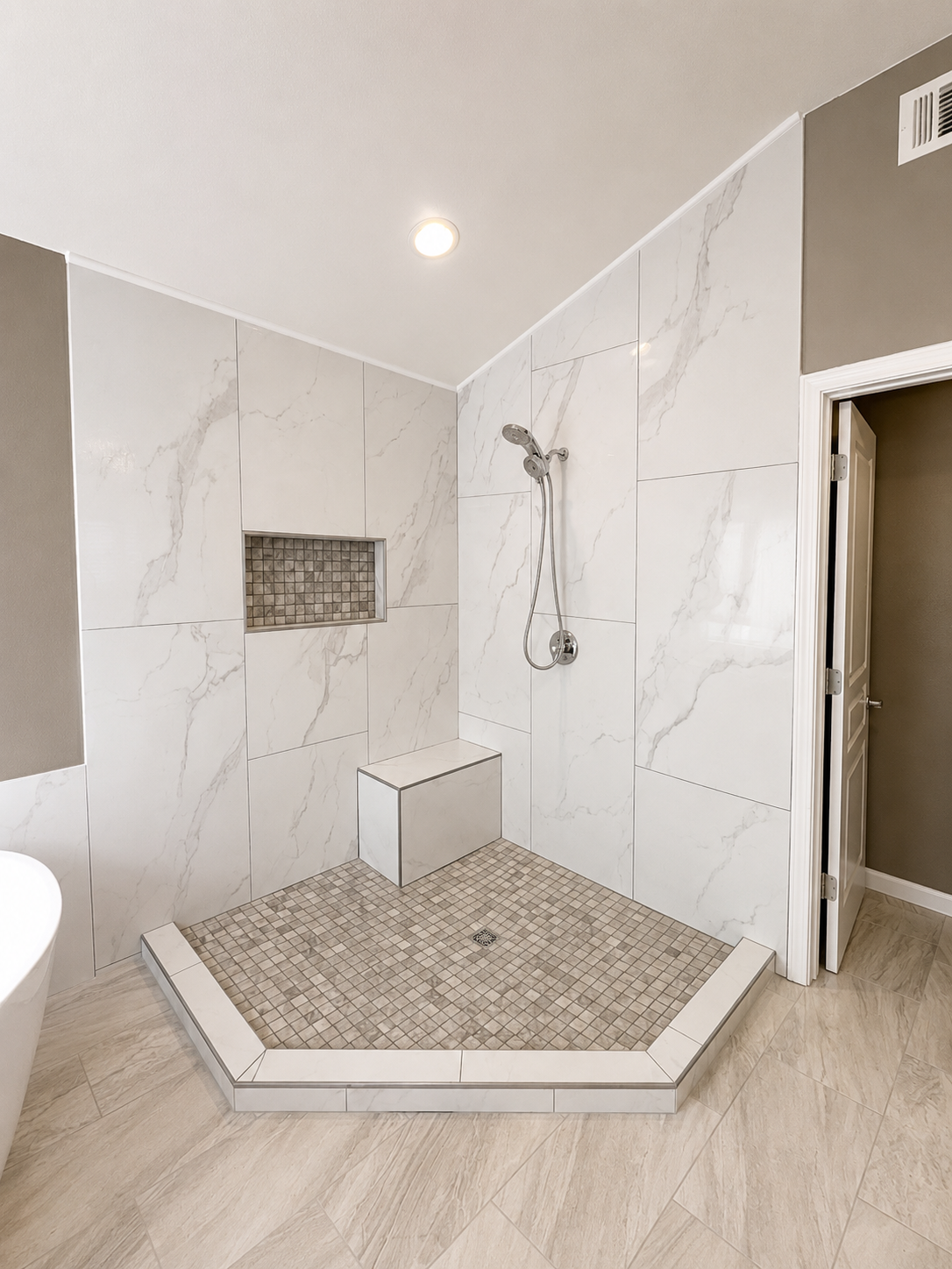 Modern bathroom shower with white marble-look tile and a built-in bench on a pebble shower floor