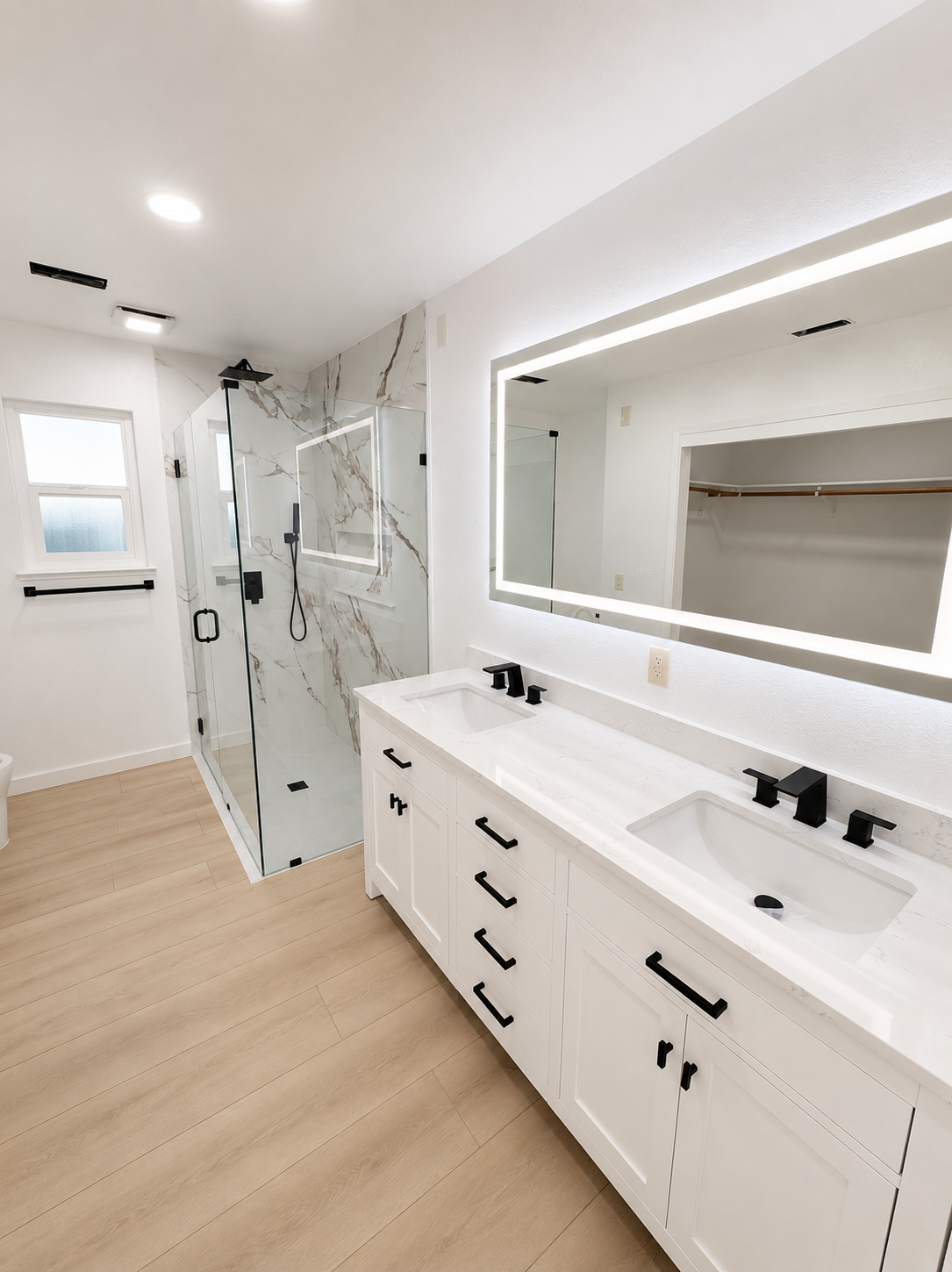 Modern white bathroom with double vanity, large mirror, glass shower, and light wood flooring