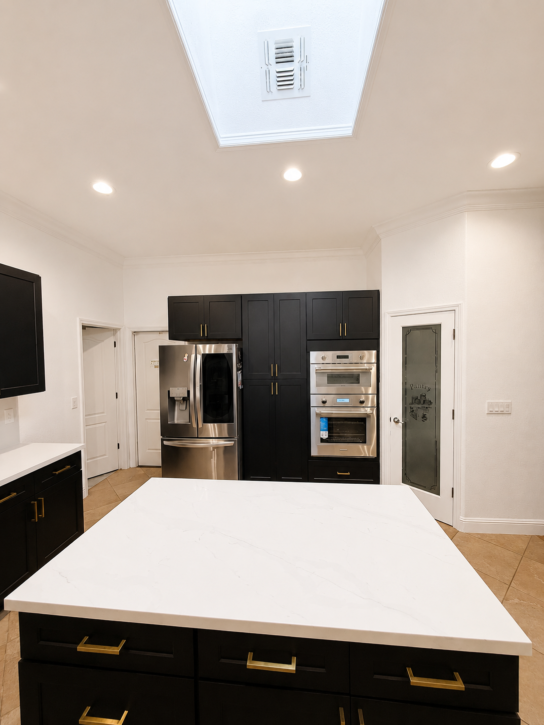 Modern kitchen with black cabinets, stainless appliances, and a large white island under a skylight.