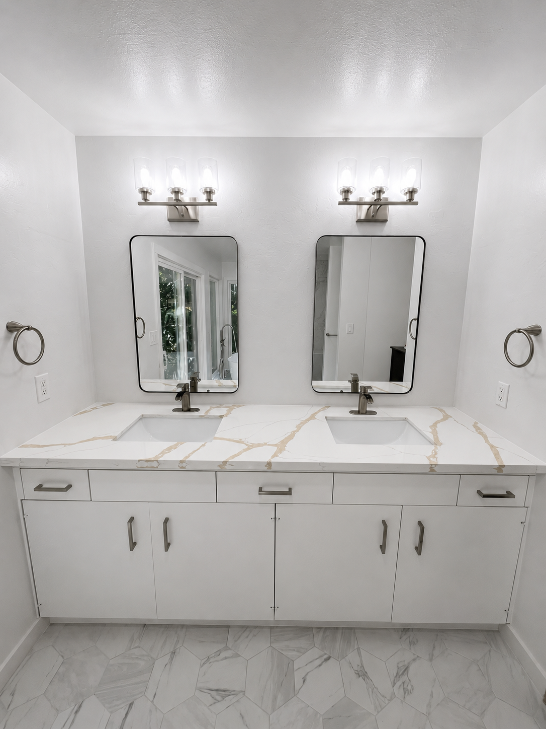 Bright white bathroom vanity with two mirrors, sinks, and chrome wall sconces.