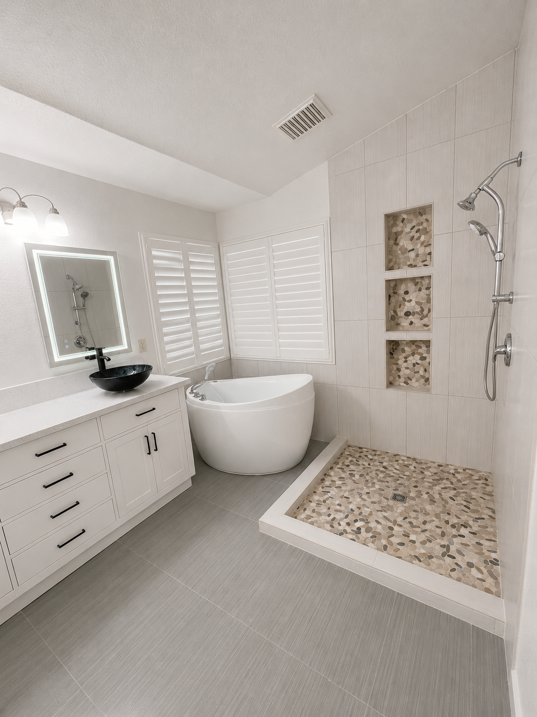 Modern white bathroom with vanity, mirror, freestanding tub, and walk-in shower with pebble tile.