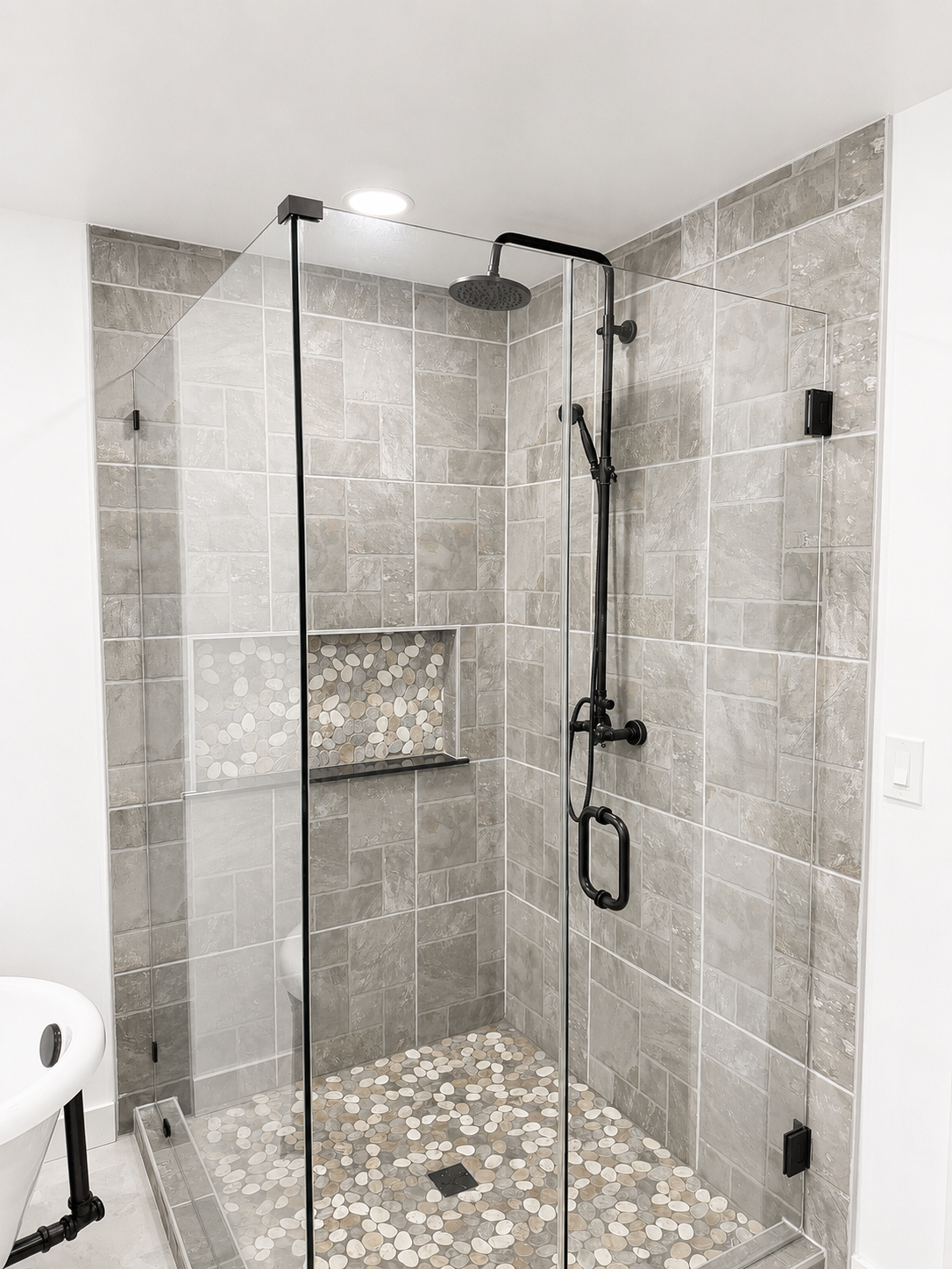Tiled walk-in shower with glass door, black fixtures, mosaic floor, and built-in niche.