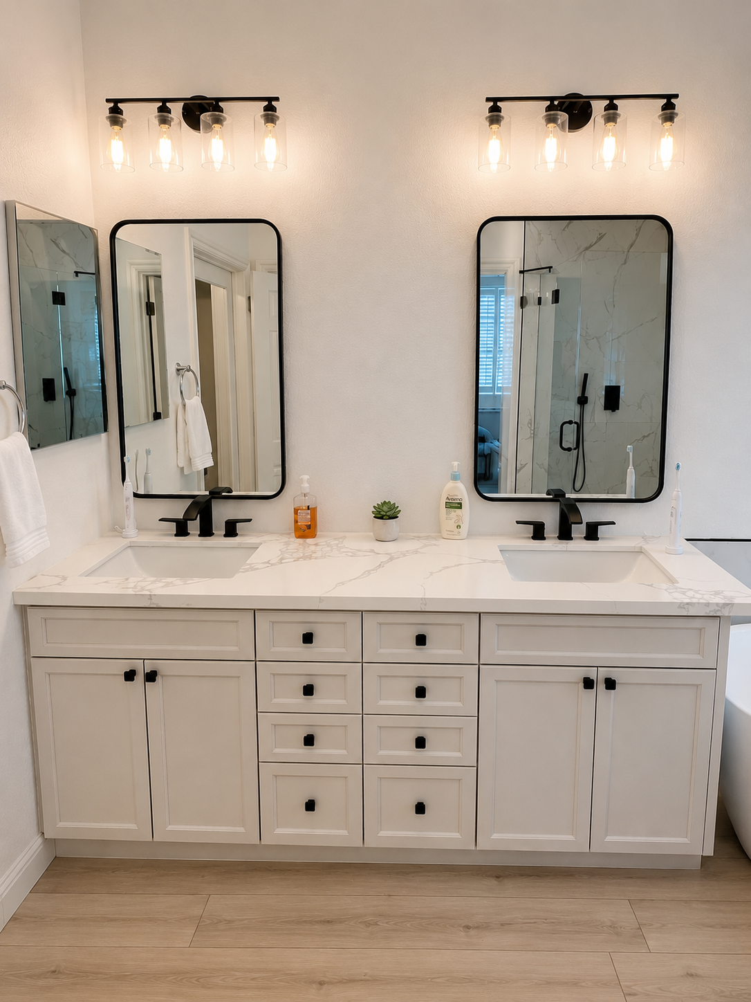 White double vanity bathroom with two mirrors, wall sconces, and light wood flooring
