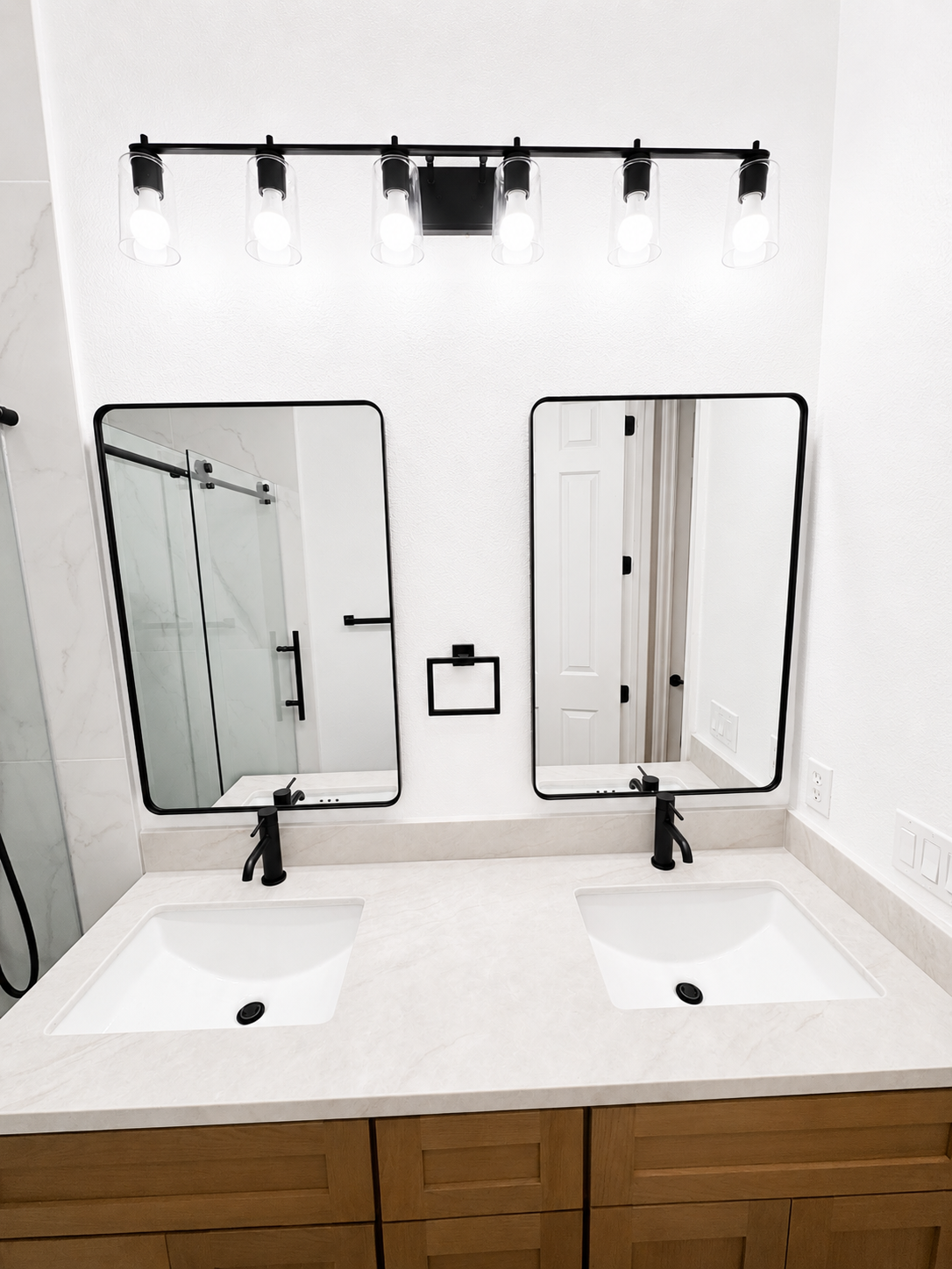 Double vanity bathroom with two mirrors, sinks, black faucets, and a glass shower visible in the reflection