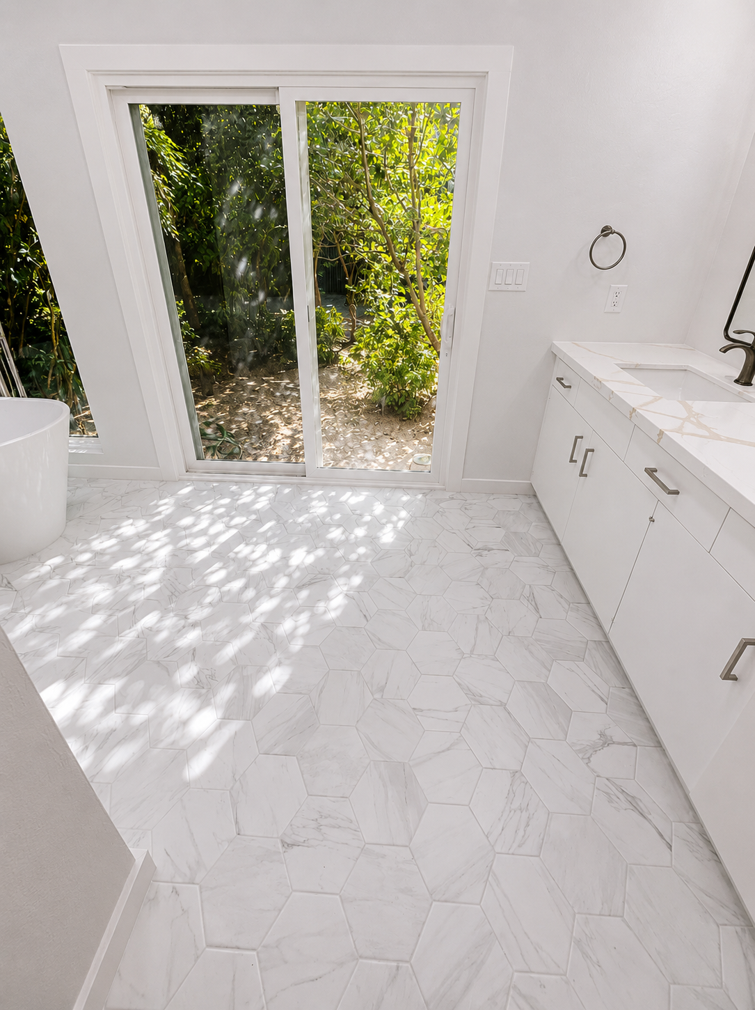 Bright bathroom with white vanity, patterned floor, and sliding glass doors to greenery outside