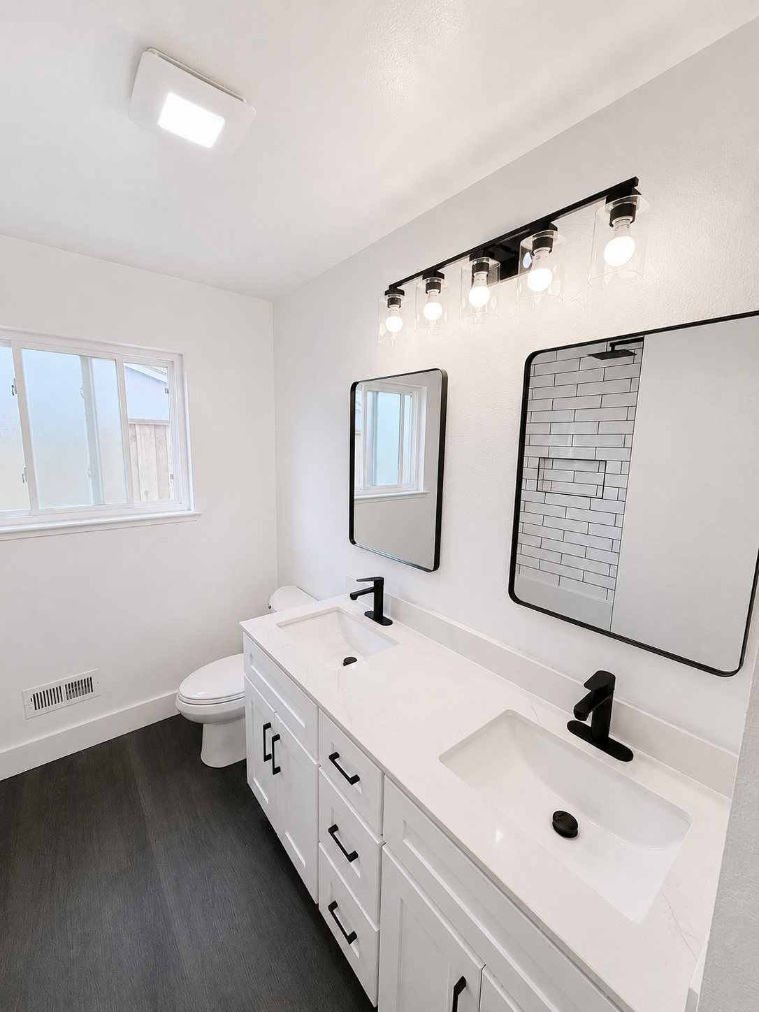Modern white bathroom with double vanity, black fixtures, and a large mirror.