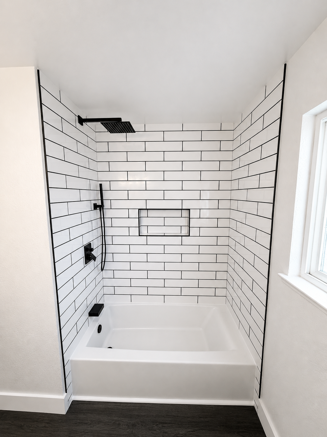 Small bathroom with a white subway-tile shower/tub and black fixtures, seen from the doorway