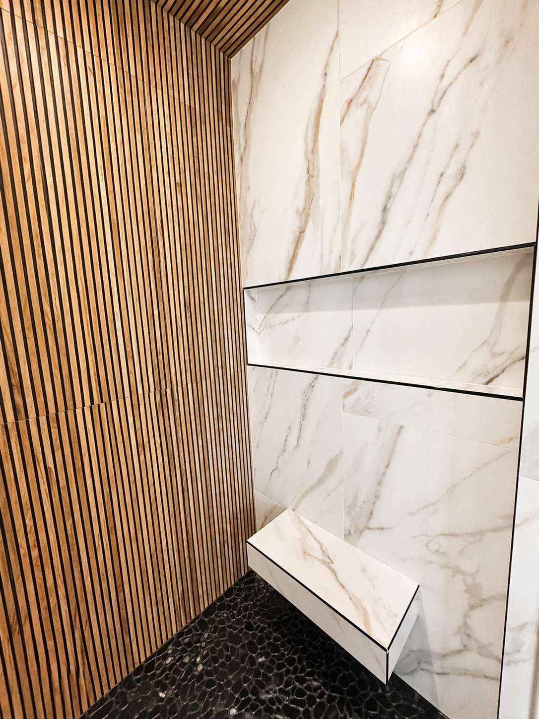Modern interior corner with wood slat wall, white marble-look panels, and a dark speckled floor.