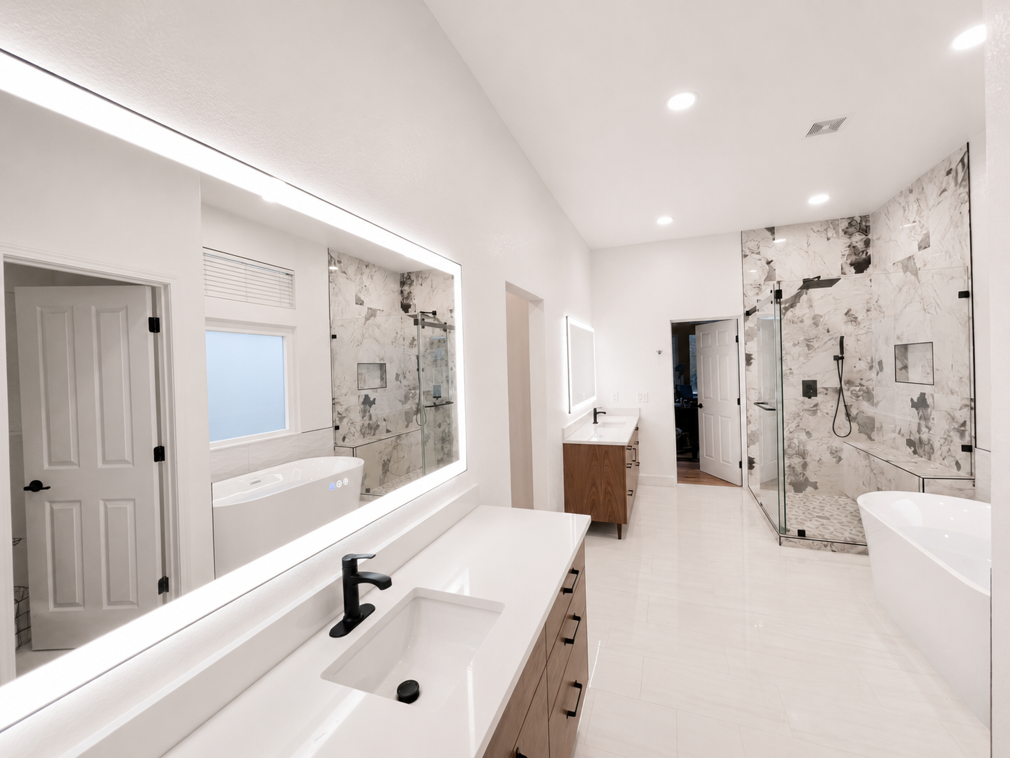 Modern white bathroom with double sinks, large mirror, walk-in shower, and freestanding tub
