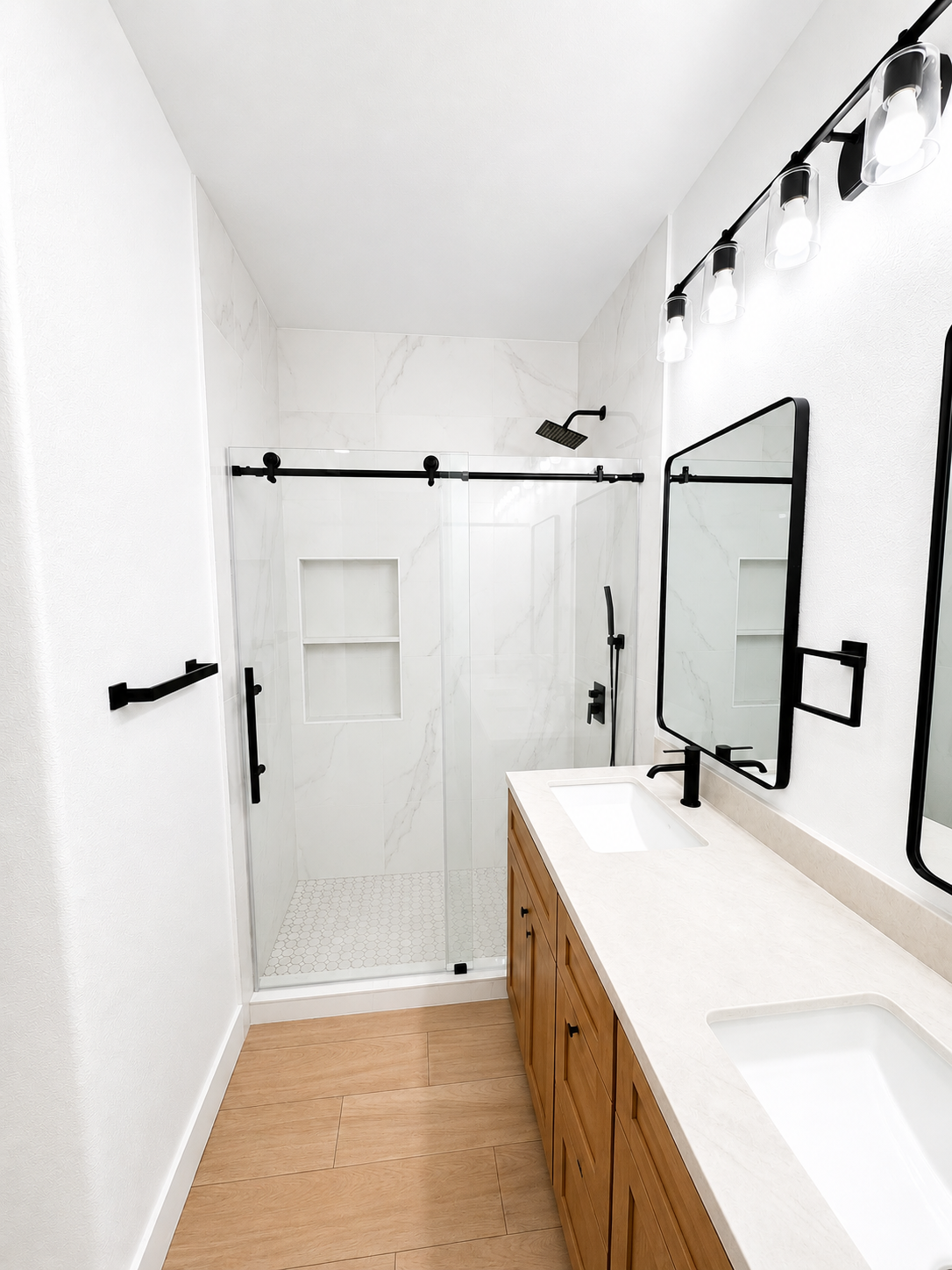 Bright modern bathroom with walk-in shower, wood vanity, white walls, and black-framed mirror.
