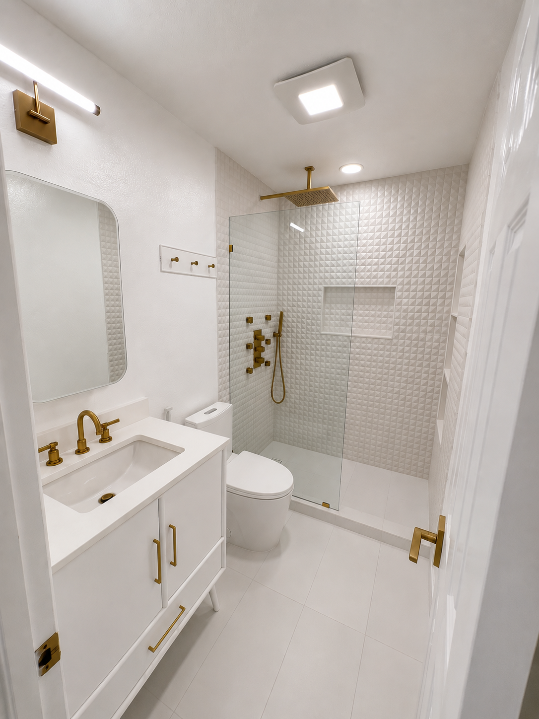 Bright white modern bathroom with gold fixtures, vanity sink, toilet, and shower stall.