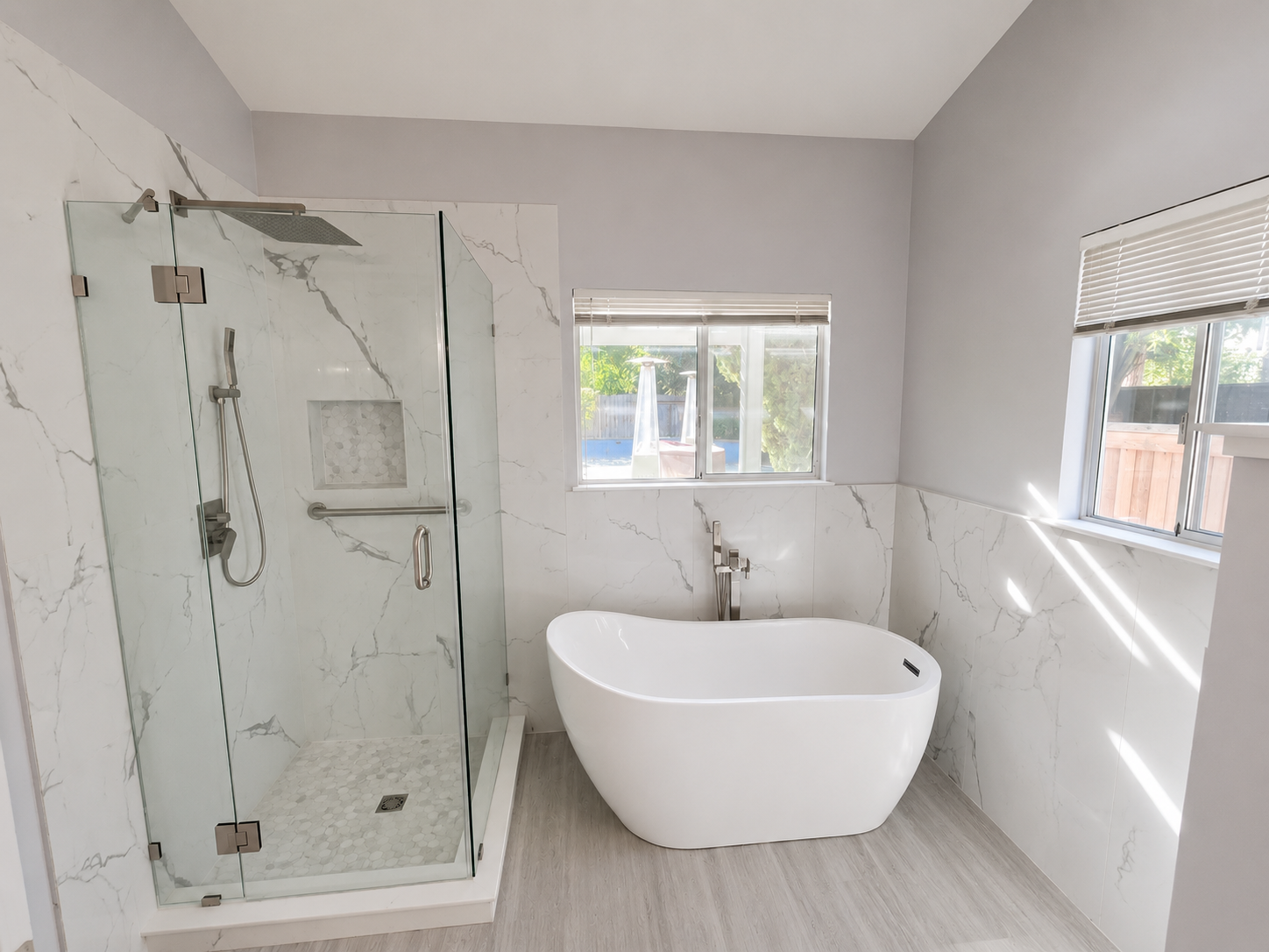 Modern bathroom with glass shower, freestanding tub, and white marble walls and floor