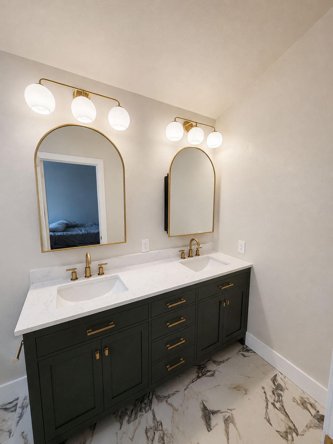 Modern bathroom vanity with double gold-framed mirrors, brass lights, dark green cabinets, and marble flooring