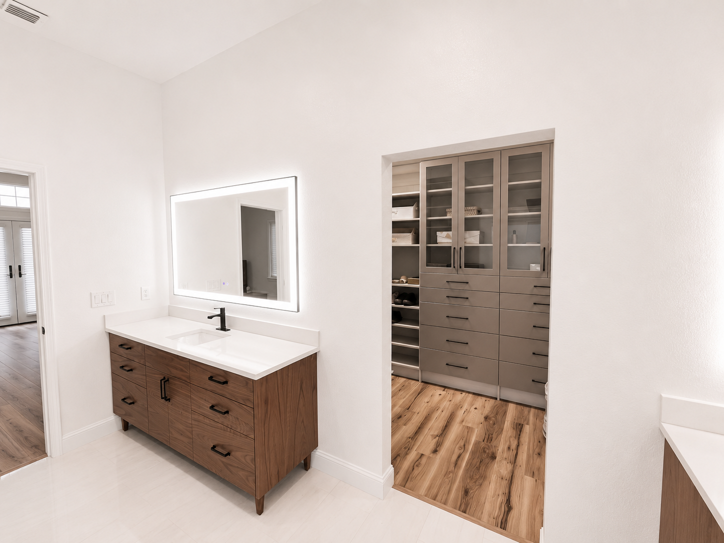 Modern bathroom with a wood vanity, white sink, mirror, and open closet with shelves and drawers.