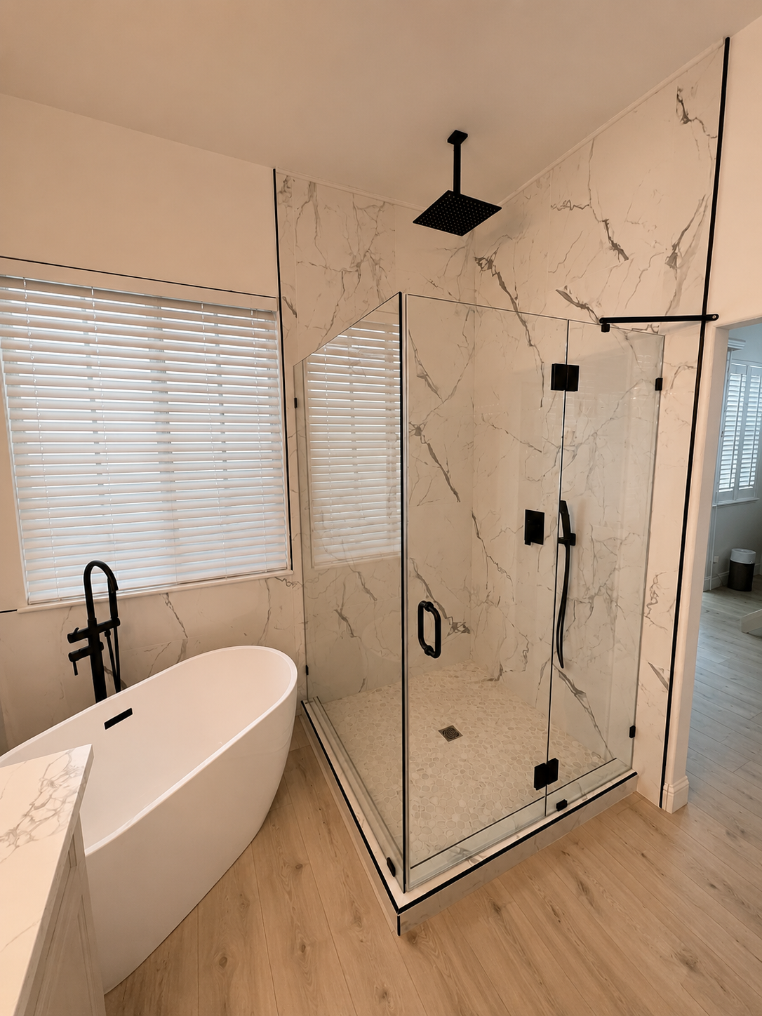 Modern bathroom with freestanding tub, glass shower, marble walls, and light wood floor
