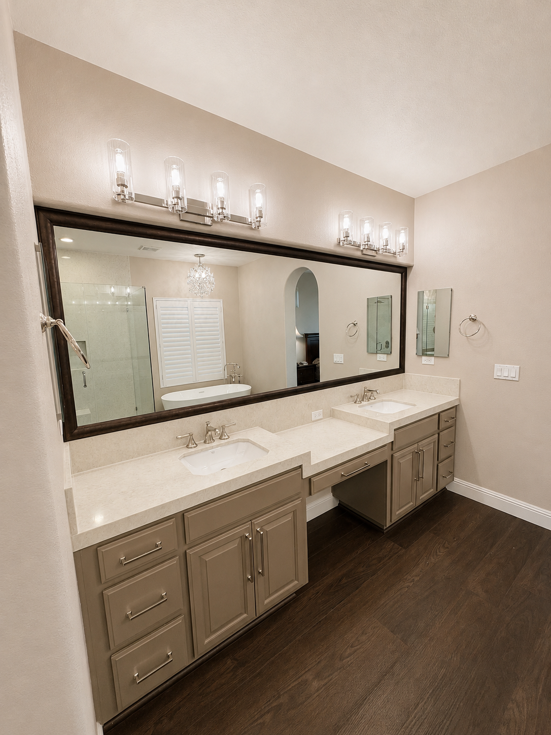 Bathroom vanity with double sinks, large mirror, and wall sconces in a beige room.
