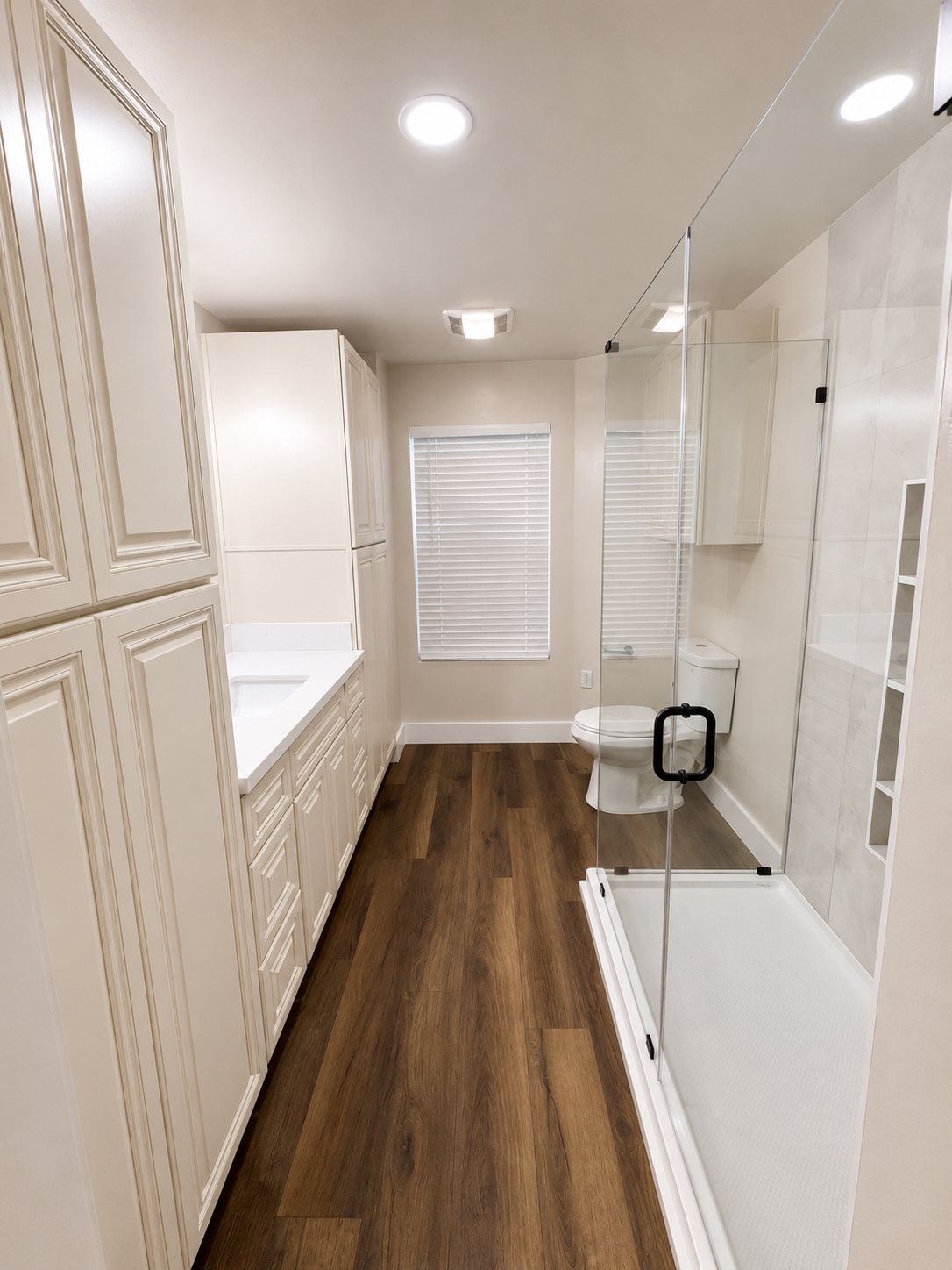 Narrow bathroom with beige cabinets, wood-look floor, and glass shower enclosure.