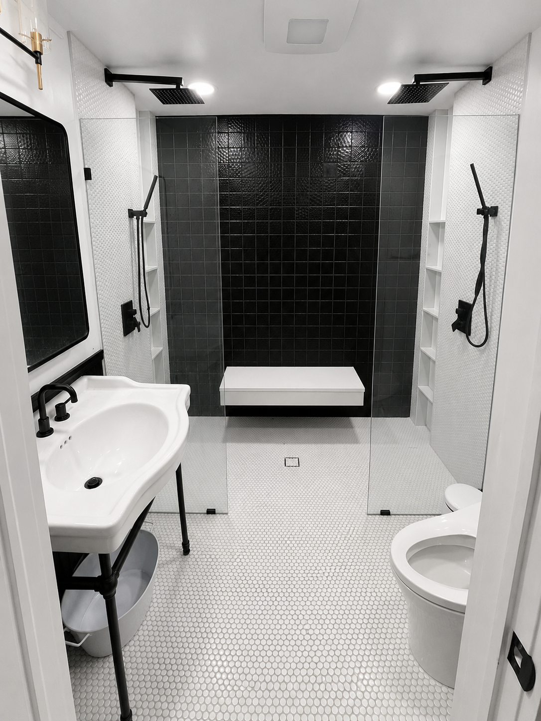 Small tiled bathroom with two sinks, wall-mounted mirrors, and a dark shower area in the center.