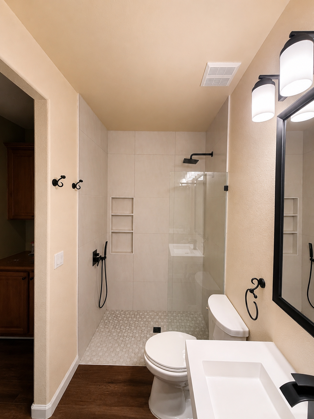 Bathroom with beige walls, white tile shower, toilet, sink, and vanity lights.