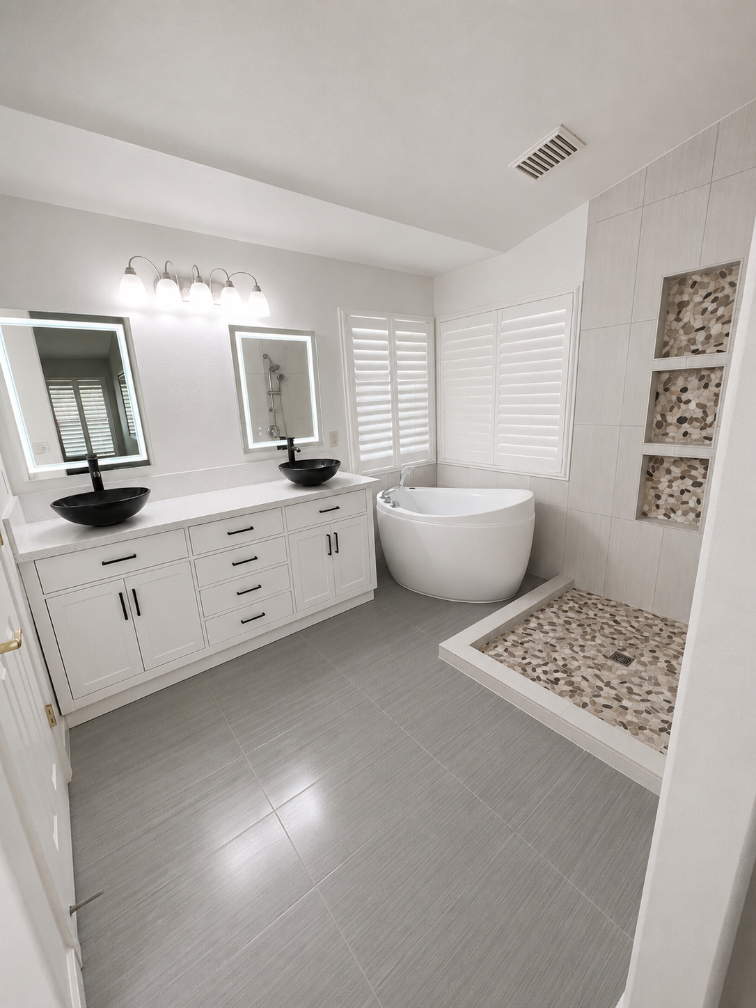 Bright white modern bathroom with double vanity, soaking tub, walk-in shower, and pebble tile floor.