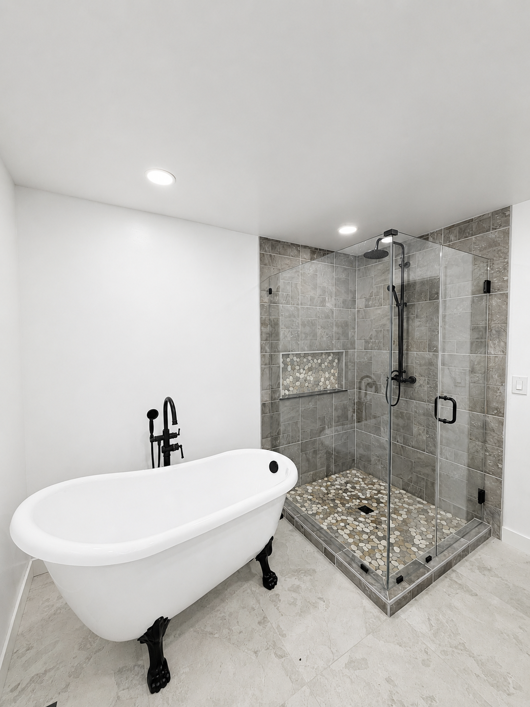 Modern bathroom with freestanding white tub, glass walk-in shower, and gray tile accents