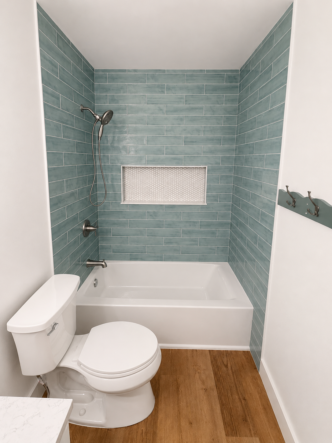 Small bathroom with teal tiled shower-tub, white toilet, and wood-look floor.