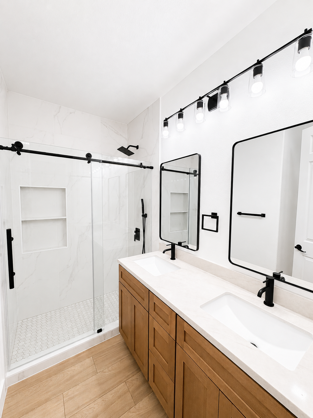 Bright modern bathroom with double vanity, mirrors, and glass shower enclosure