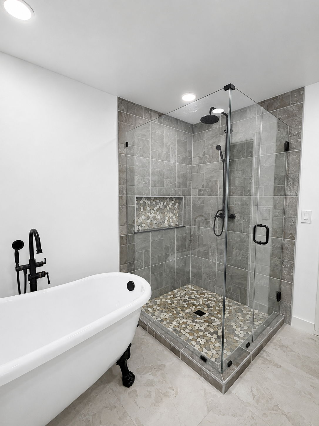 Modern bathroom with a freestanding tub and a glass-enclosed tiled shower with pebble floor.